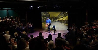 A man on stage with an acoustic guitar bowing to an applauding audience