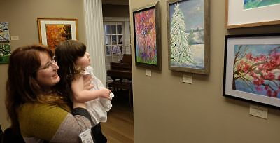 Woman holding young girl in her arms looking at paintings at Galena Center for the Arts